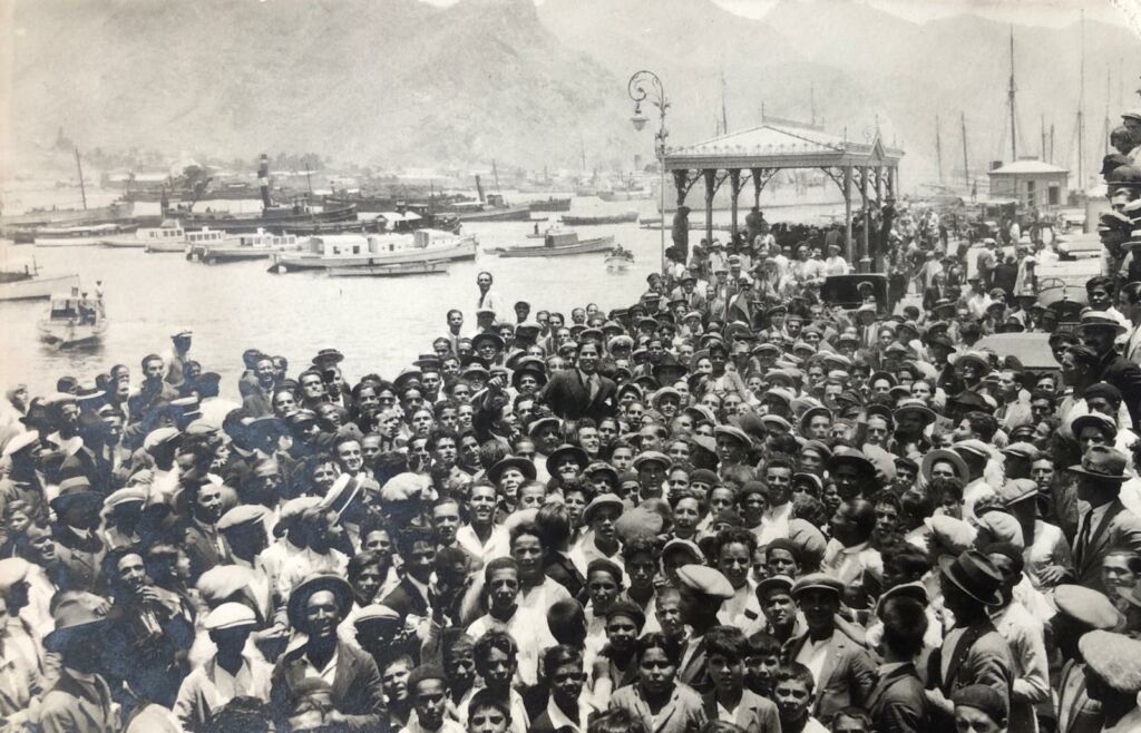 Centenares de aficionados, congregados el 10 de julio de 1928 en la vieja marquesina del puerto de Santa Cruz de Tenerife para recibir a Ángel Arocha, que aparece izado a hombros en el centro de la foto (FONDO CDT/LEGADO AROCHA)